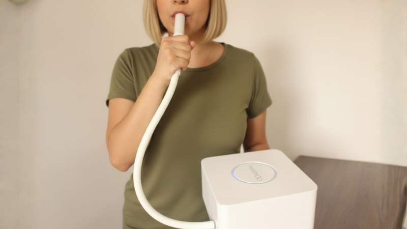 Mulher realizando teste respiratório para SIBO, soprando em coletor conectado ao aparelho